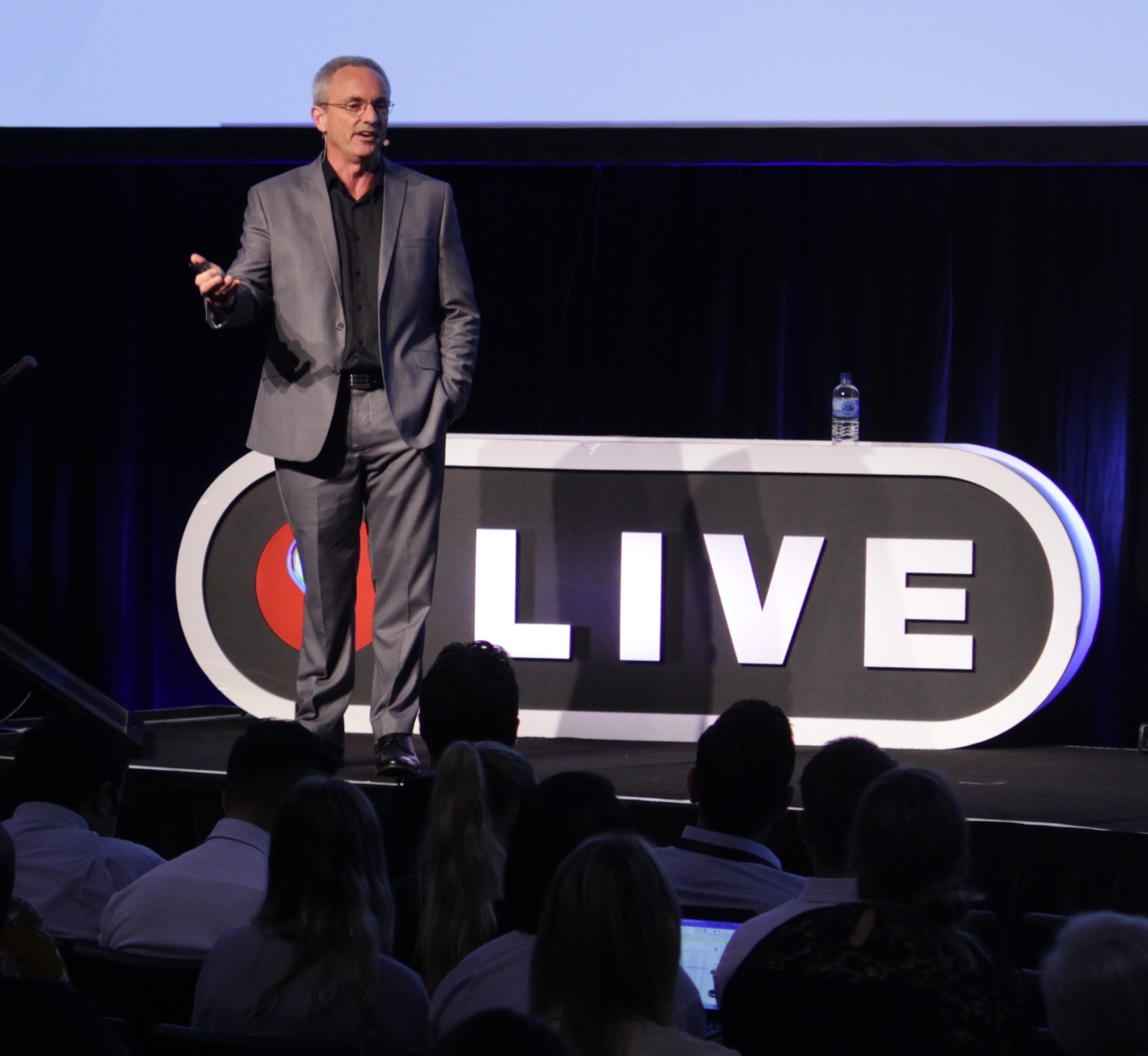 A presenter speaking on stage to a large conference audience